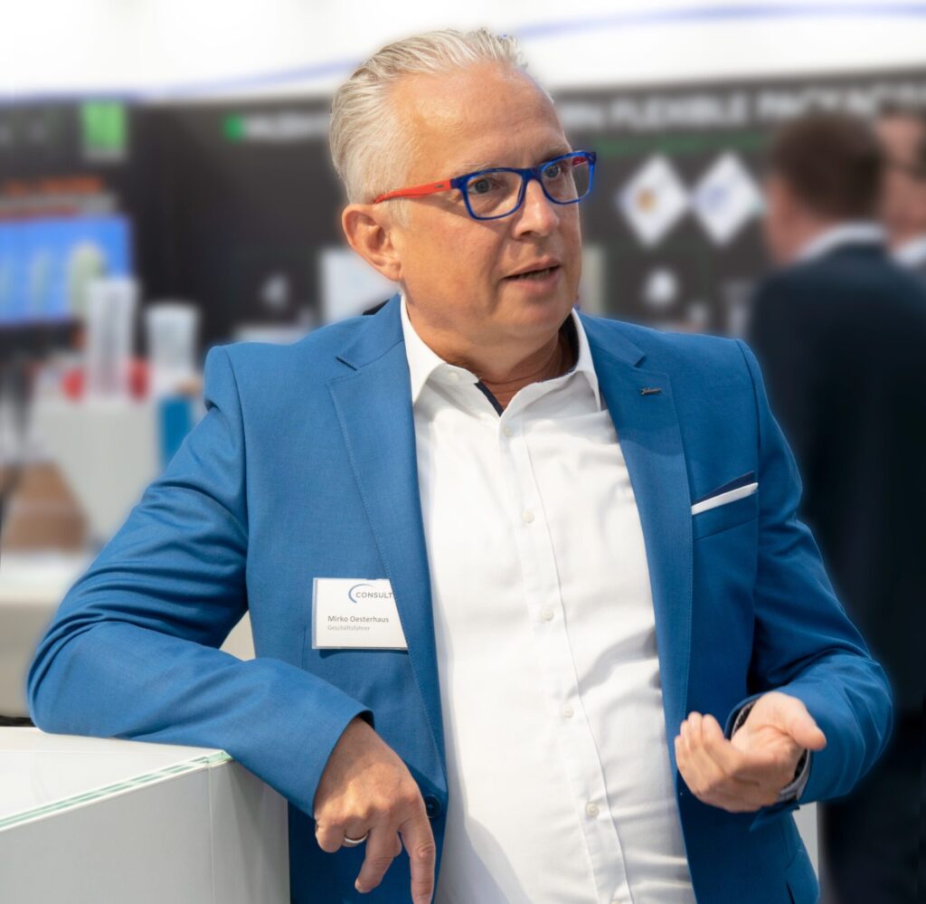 Mirko Oesterhaus in blauem Anzug und weißem Hemd spricht gestikulierend auf der Hannover Messe.
