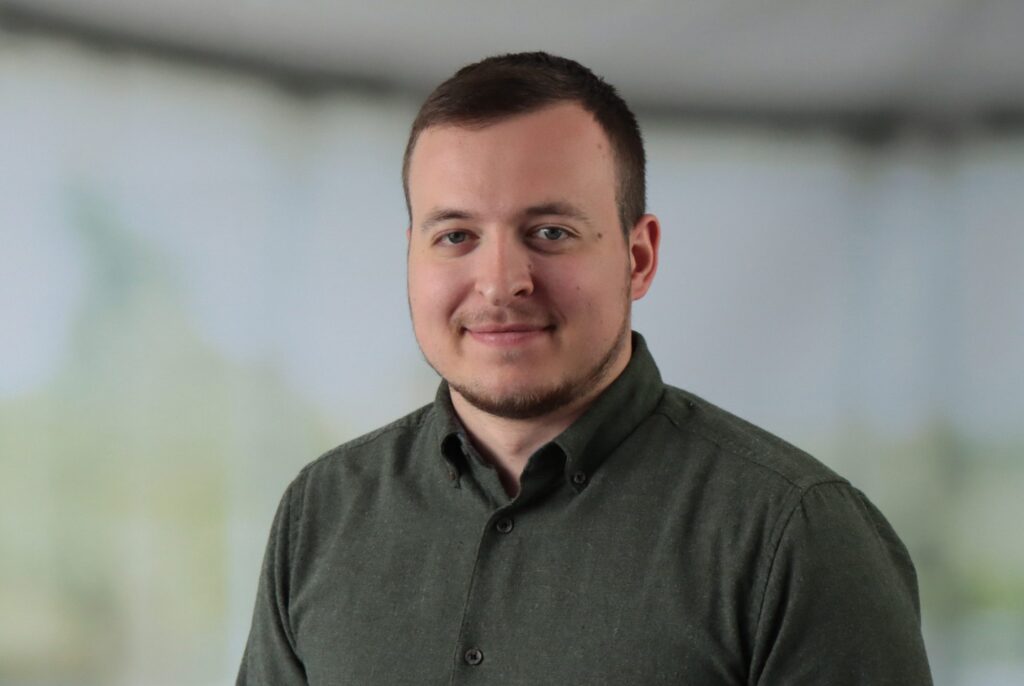 Business-Porträt von Marc Alsdorf in grünem Hemd vor grauem Hintergrund.