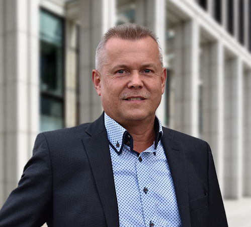 Sven Kaiser, in Anzug und Hemd, steht draußen vor einem modernen Bürogebäude und blickt freundlich in die Kamera.